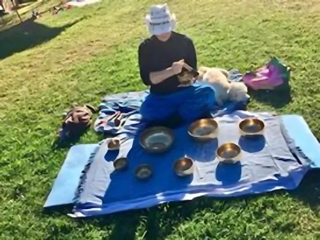 Lady sitting on a mat in a park doing therapy with the Tibetan Singing Bowls.