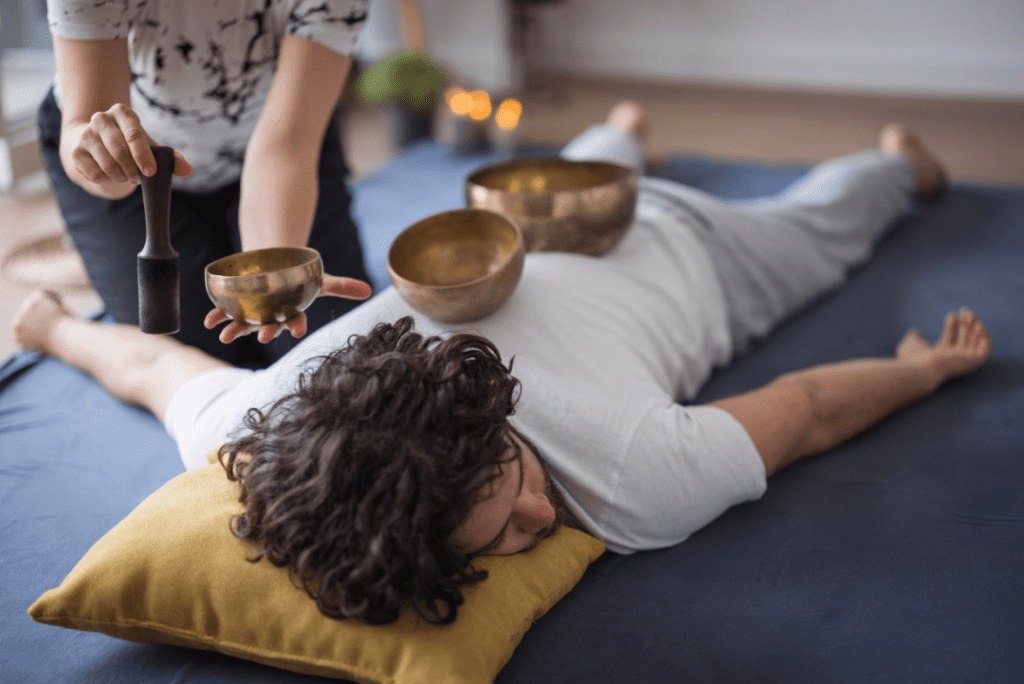 male person laying on his stomach with sound bowls on his back getting therapy