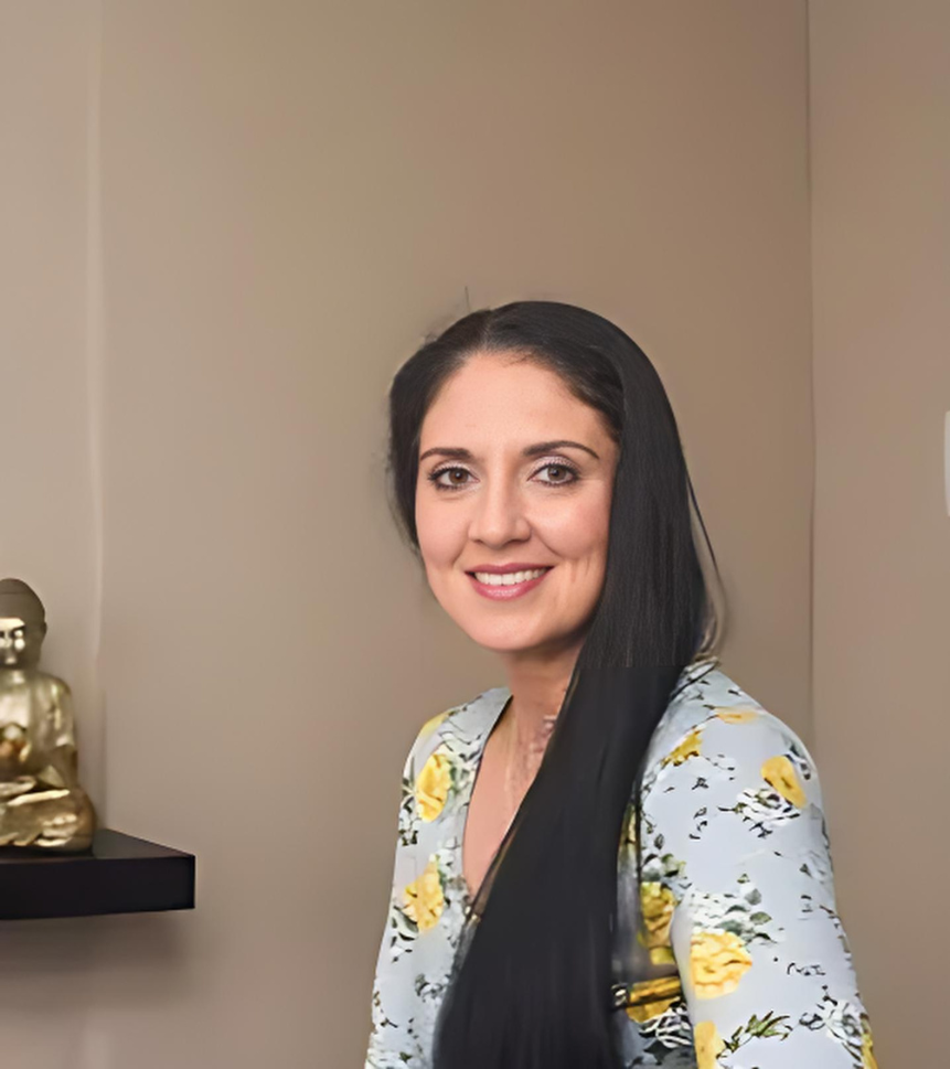 A woman with long black hair standing in front of a cream-coloured wall. Buddha statue on a rack.